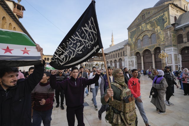 En maskerad krigare bär HTS (Hayat Tahrir al-Sham) flagga i Damaskus den 10 december.  