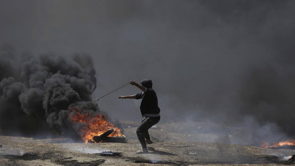 Palestinier redo att slunga iväg en sten i samband med måndagens våldsamma protester vid Gazagränsen.