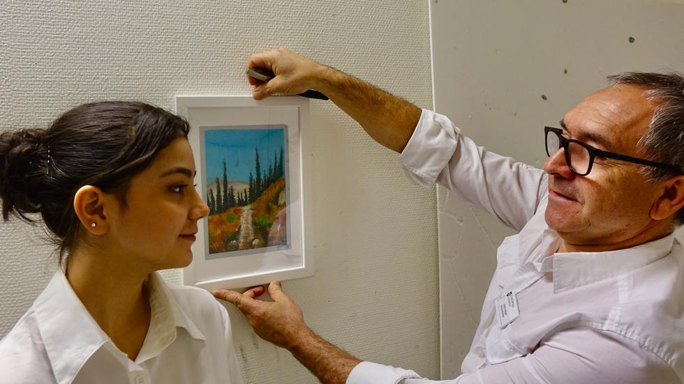 Fatima Hassani får hjälp av sin lärare Mario Rojas att hänga en av sina bilder på Kulturskolans elevutställning.