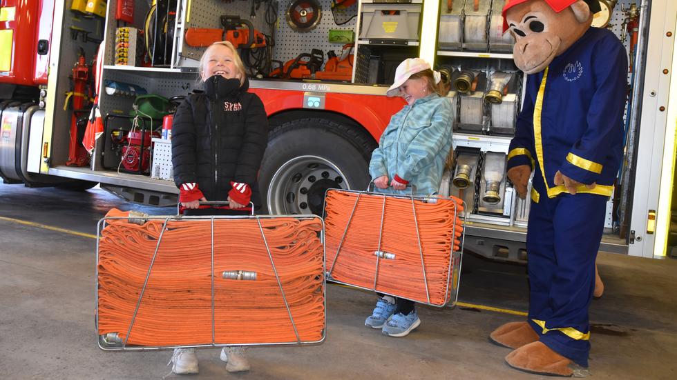 Räddningstjänstens maskot Flammy kollar in när Agnes Ask och Juni Blomqvist testar att bära de väskor med slangar som en brandman behöver kunna. "Ganska tungt", konstaterar de båda 9-åringarna. 