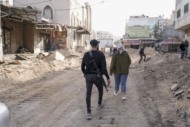 En beväpnad palestinier går omkring på en väg i Jenin som tog stor skada vid helgens israeliska operation där.