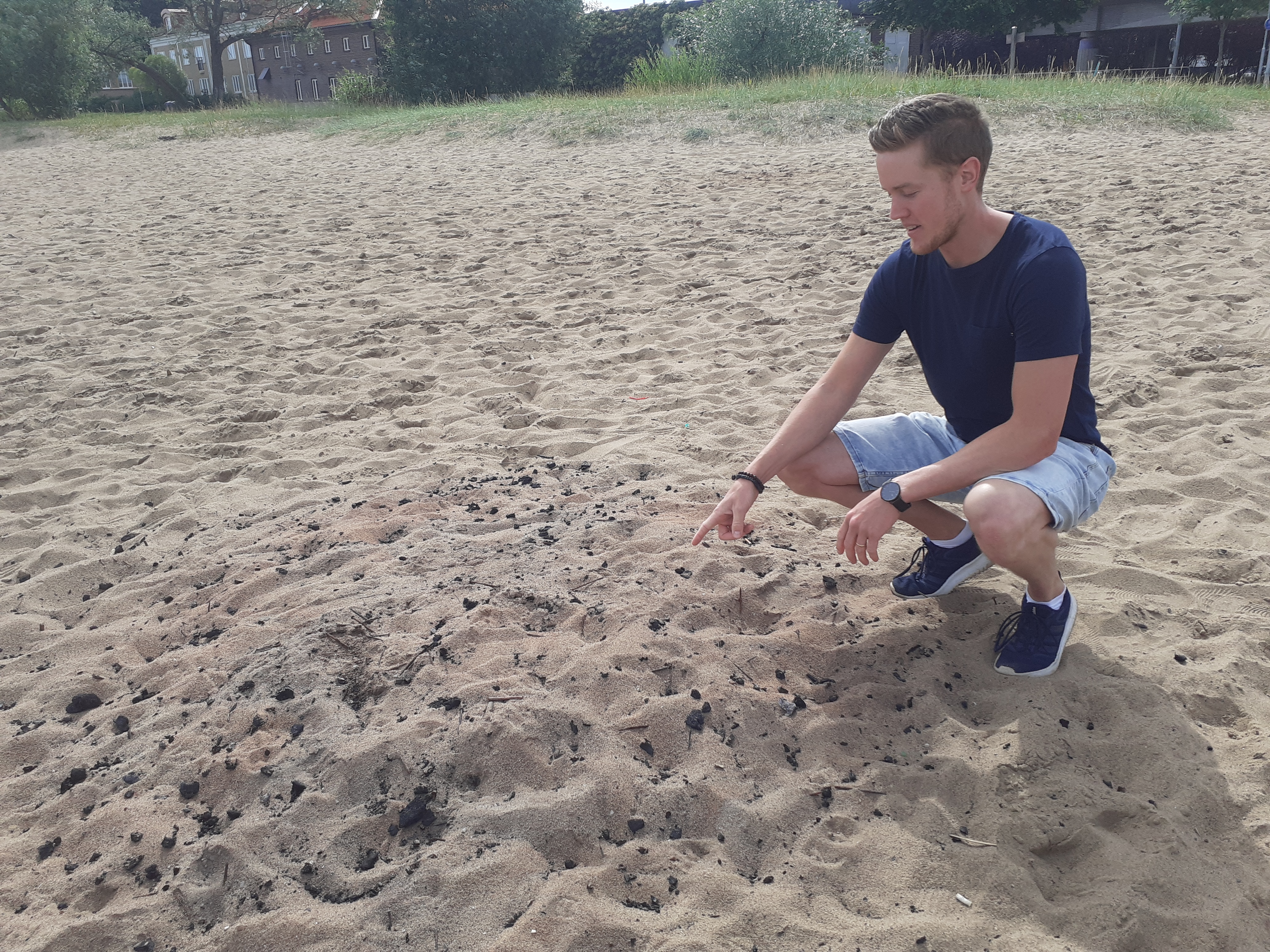 Arvid Nilsson visar att någon har försökt gömma sin gamla grillkol i sanden.