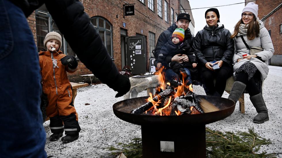 Charlie Grönhage festar loss på en grillad marshmallow medan Fredrik Jergefelt (med sonen Elis i knät), Ame Ogbomo och Lucie Güber värmer sig framför brasan. 