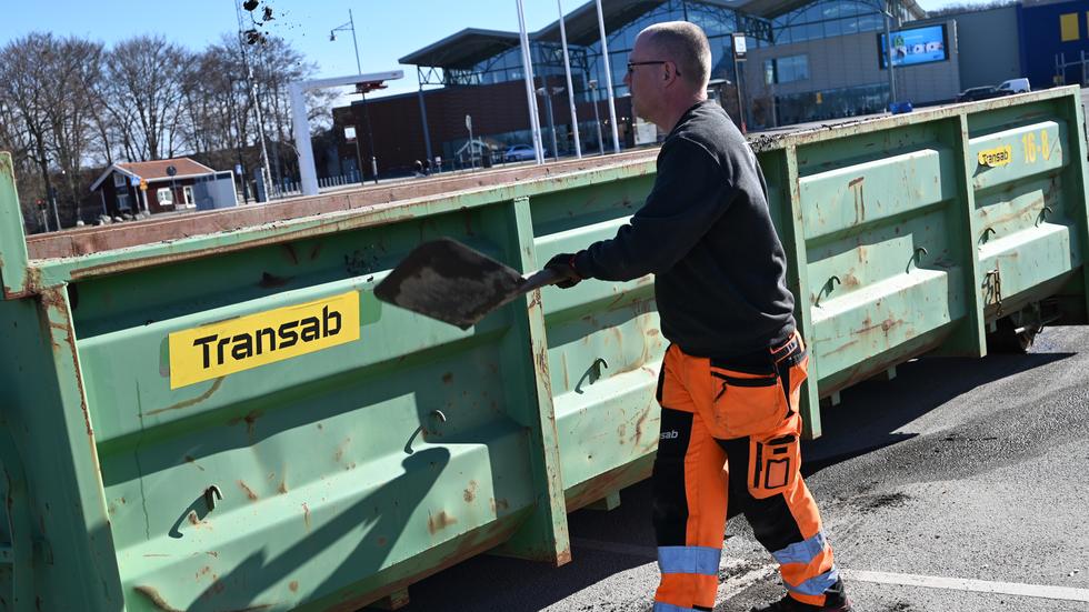 Mattias Svensson använder en spade för att få upp det skräp som ramlat utanför containern.