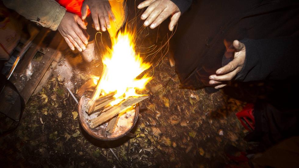Tiggare som bosatt sig i en park i Malmö värmer sig vid elden.
