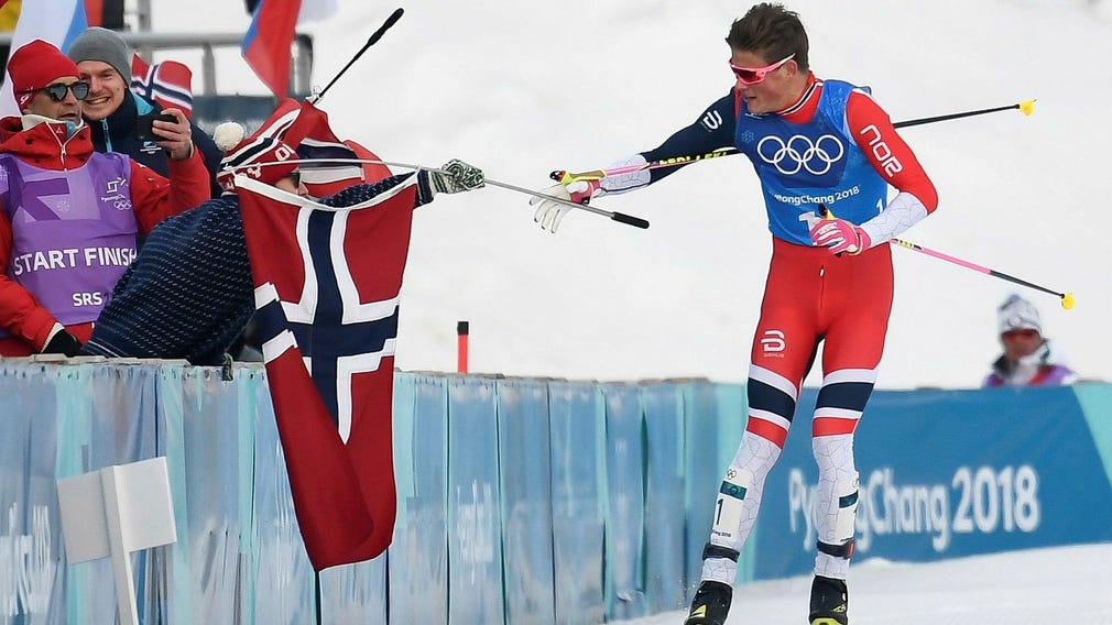 Johannes Høsflot Klæbo tar med en flagga i mål till stafettsegern i OS 2018.