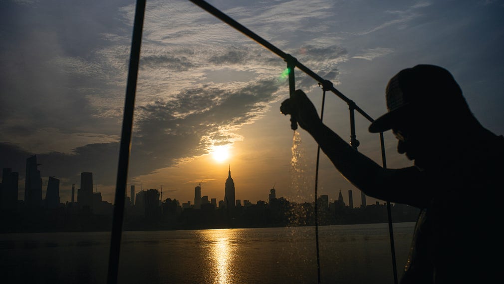 En man svalkar sig med vatten på en pir i New Jersey medan solen stiger över Manhattan under värmeböljan i juli 2019.