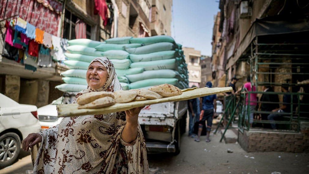 Hoda Nasser bär hem dagens ranson av bröd – fem för henne, fem för maken. Bröden är subventionerade av staten och kostar Hoda sammanlagt 50 piastrar eller motsvarande 60 öre. I bakgrunden en lastbil fullastad med vetesäckar.