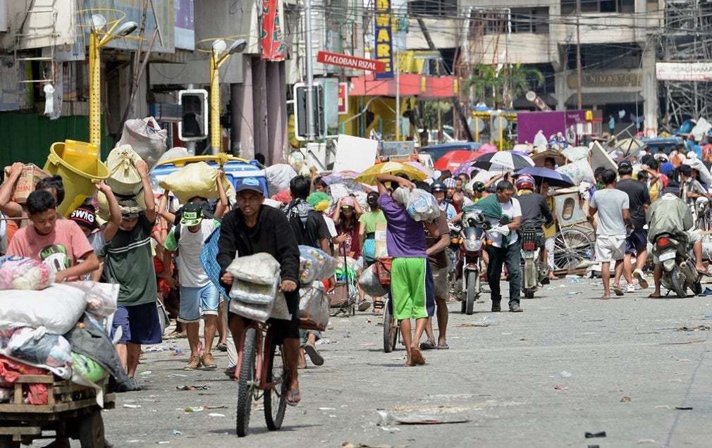 Desperata boende i Tacloban bär hem mat, vatten och andra förnödenheter som plundrats från butiker i staden på söndagen.
