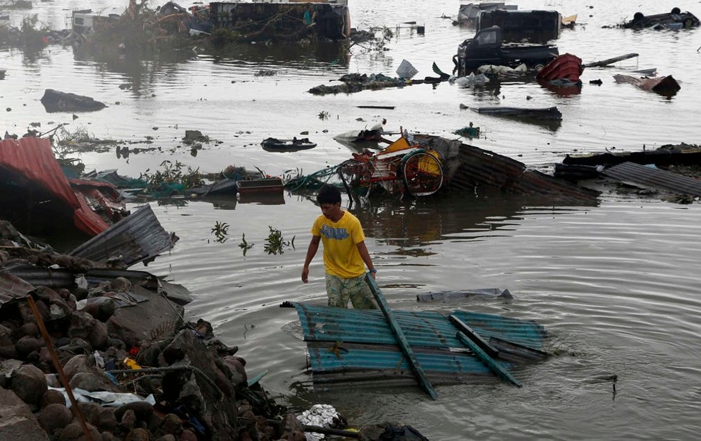 En man lyfter ett tak ur vattnet i Tacloban.