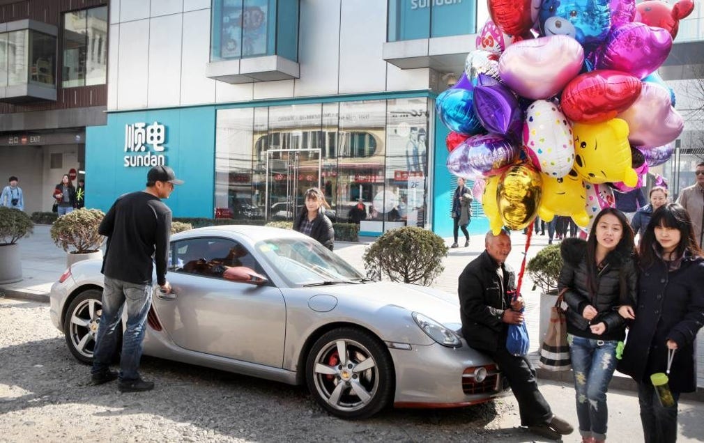 Ballongförsäljare Li sitter kvar på motorhuven till en felparkerad Porsche trots att ägaren skrikit att det är hennes bil.