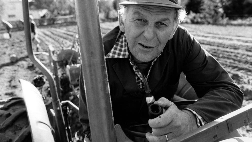 1985. Centerpartiets ledare Thorbjörn Fälldin på sin traktor med pipa i handen på lantbruket i Ramvik norr om Härnösand.