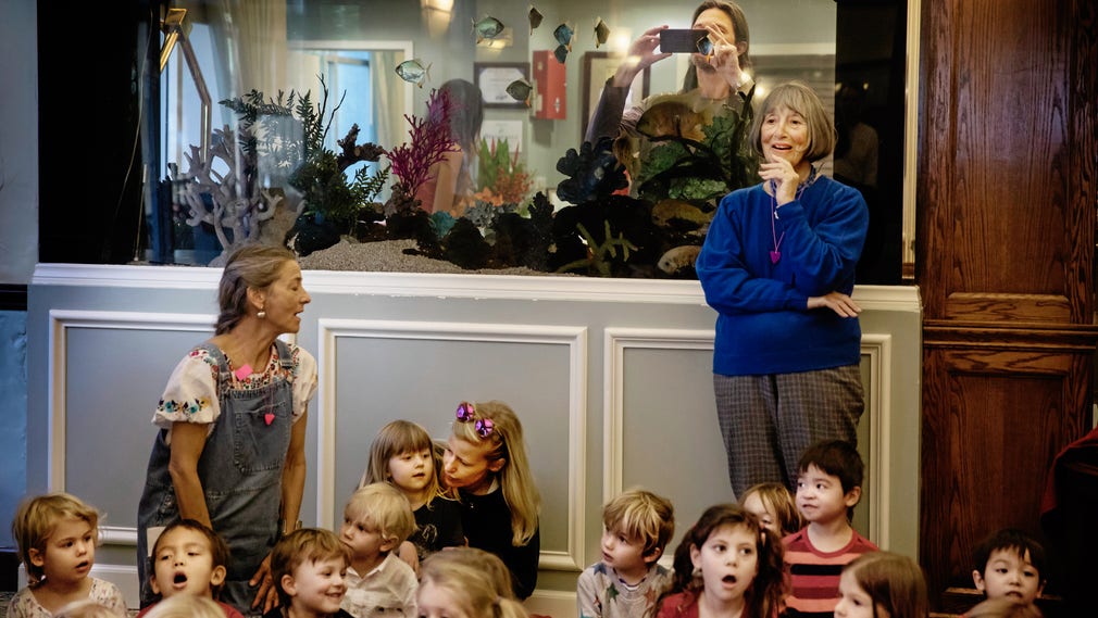 Linus Sandgren fotograferar genom akvariet när dottern Lucys förskola framträder på ett seniorboende på Alla hjärtans dag. Förskoleföreståndaren Ina Sinsheimer (i blått) är 88 år. Varje dag kör hon till skolan i sin Jaguar.