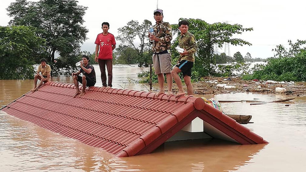 Människor stående på ett hustak i en by som översvämmades av dammkollapsen.