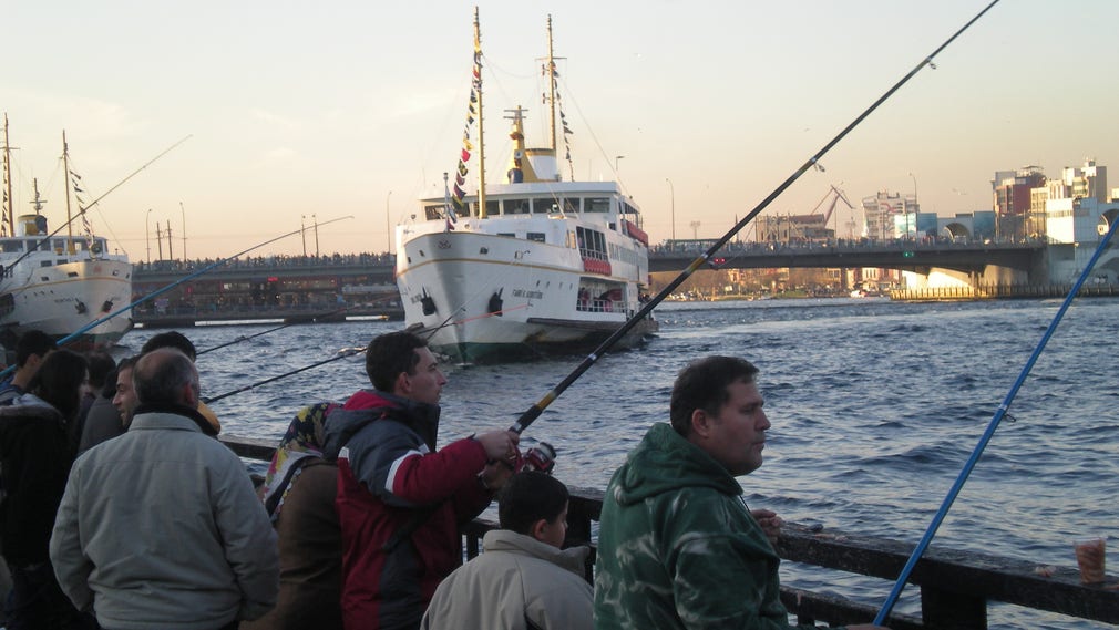 Några fiskare i Istanbul hoppas på napp mitt i den intensiva båttrafiken. I bakgrunden Galatabron fullproppad med människor och biltrafik.
