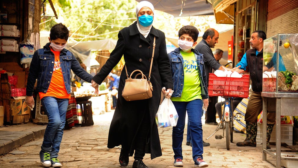 En syrisk kvinna och hennes två söner på en marknad i huvudstaden Damaskus – där munskydd blivit en allt vanligare syn.