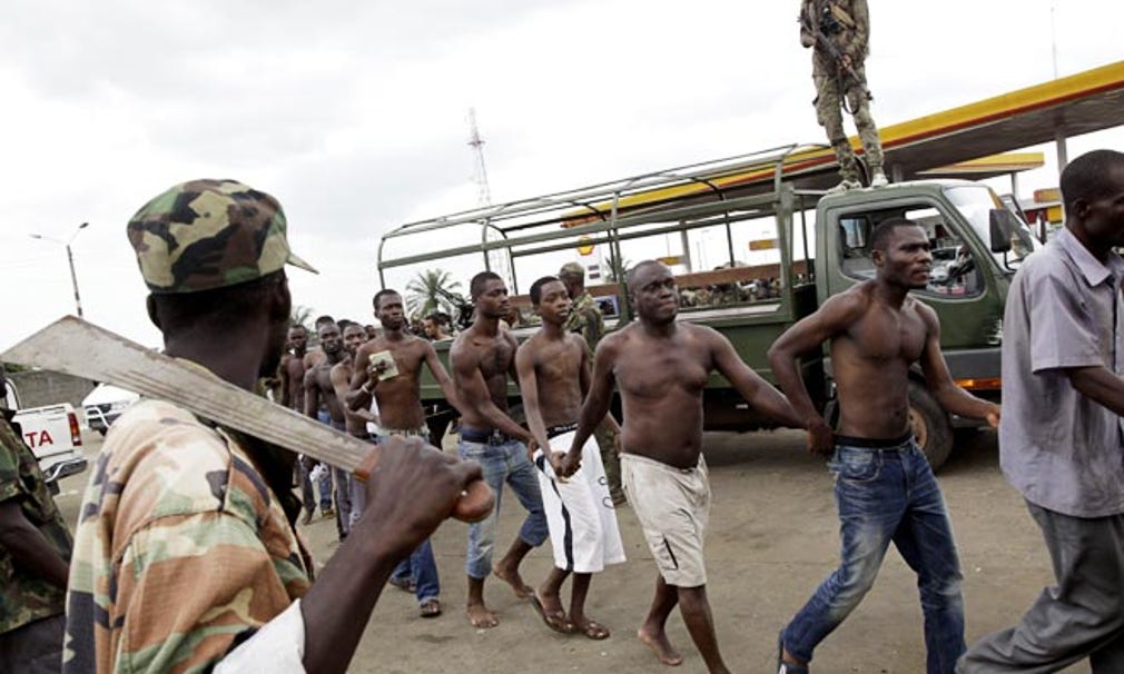 Män som tillfångatagits av okänd anledning bevakas av Ouattaratrogna soldater vid en av infarterna till Abidjan.