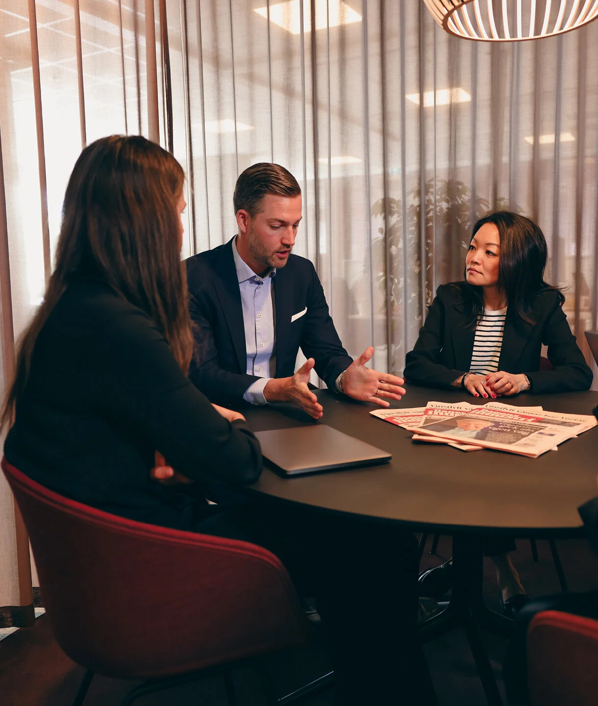 en grupp affärsmänniskor som sitter runt ett bord och diskuterar med flera kopior av Dagens industris tidning liggandes på bordet